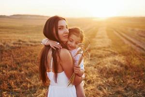 Positive little girl with her mother have weekend outdoors on the summer field together photo