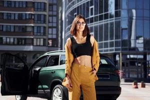 edificio de negocios moderno en segundo plano. joven mujer de moda con abrigo de color burdeos durante el día con su coche foto