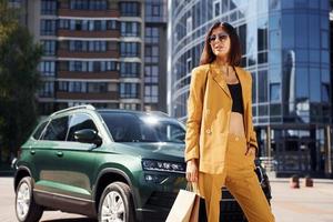 Young fashionable woman in burgundy colored coat at daytime with her car photo