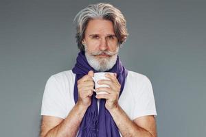 Getting sick. Against grey background. Stylish modern senior man with gray hair and beard is indoors photo