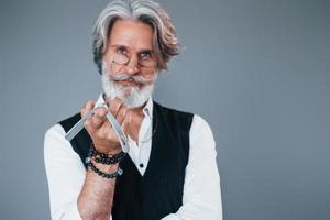 Barbershop tools. Against grey background. Stylish modern senior man with gray hair and beard is indoors photo