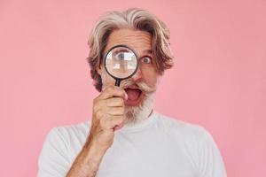 Using magnifying glass. Stylish modern senior man with gray hair and beard is indoors photo