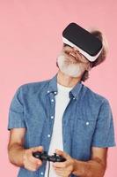 Playing game with virtual reality glasses and joystick. Stylish modern senior man with gray hair and beard is indoors photo