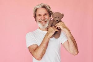 Holds teddy bear. Stylish modern senior man with gray hair and beard is indoors photo