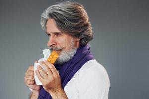 Getting sick. Against grey background. Stylish modern senior man with gray hair and beard is indoors photo