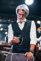 In retro clothes in barbershop. Stylish modern senior man with gray hair and beard is indoors photo