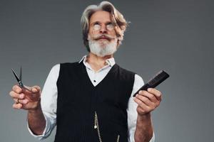 Barbershop tools. Against grey background. Stylish modern senior man with gray hair and beard is indoors photo