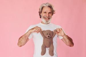 tiene oso de peluche. un anciano moderno y elegante con pelo gris y barba está en el interior foto