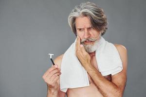 concepción del afeitado. un anciano moderno y elegante con cabello gris y barba está en el interior foto