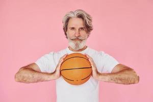 With sport ball in hands. Stylish modern senior man with gray hair and beard is indoors photo