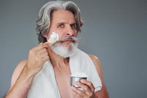 With shaving gel. Stylish modern senior man with gray hair and beard is indoors photo