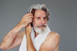 Taking care of face and skin clearness. Stylish modern senior man with gray hair and beard is indoors photo
