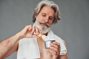 con gel de afeitar. un anciano moderno y elegante con cabello gris y barba está en el interior foto