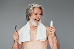 Using toothpaste. Stylish modern senior man with gray hair and beard is indoors photo