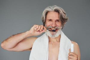 Using toothpaste. Stylish modern senior man with gray hair and beard is indoors photo