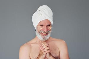 con toalla blanca en la cabeza. un anciano moderno y elegante con cabello gris y barba está en el interior foto