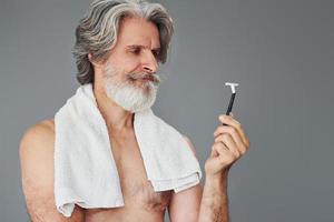 concepción del afeitado. un anciano moderno y elegante con cabello gris y barba está en el interior foto