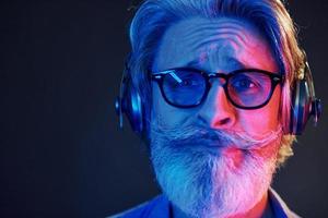 Close up portrait. Neon lighting. Stylish modern senior man with gray hair and beard is indoors photo