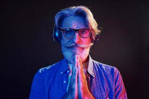 Neon lighting, conception of party. Stylish modern senior man with gray hair and beard is indoors photo