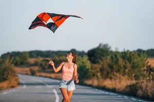 Young cheerful woman having fun with kite outdoors on the road photo