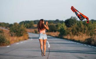 joven mujer alegre divirtiéndose con cometa al aire libre en la carretera foto