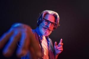 Neon lighting. In headphones. Stylish modern senior man with gray hair and beard is indoors photo