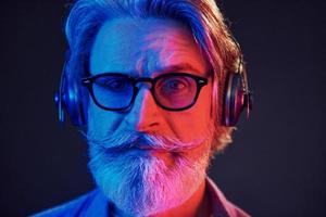 Close up portrait. Neon lighting. Stylish modern senior man with gray hair and beard is indoors photo