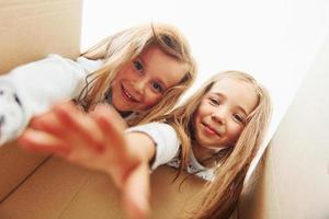 Looking inside of paper box. Two cute little girls indoors at home together. Children having fun photo