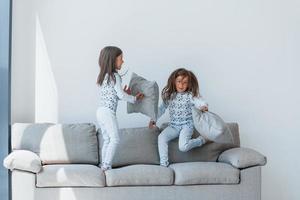 Pillow fight. Two cute little girls indoors at home together. Children having fun photo