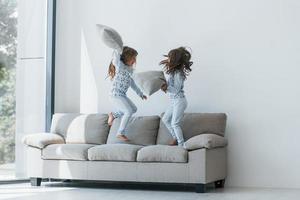 Pillow fight. Two cute little girls indoors at home together. Children having fun photo