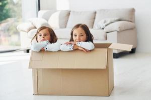 Sitting in the paper box. Two cute little girls indoors at home together. Children having fun photo