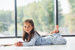 Lying on the floor and drawing. Cute little girl indoors at home alone photo