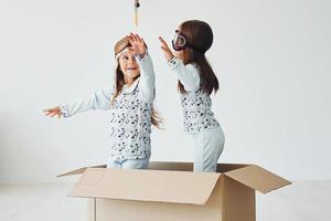 Sitting in the paper box. Two cute little girls indoors at home together. With retro pilot glasses and hat photo