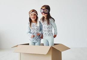 Sitting in the paper box. Two cute little girls indoors at home together. With retro pilot glasses and hat photo