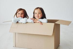 Sitting in the paper box. Two cute little girls indoors at home together. Children having fun photo