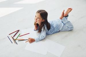 Lying on the floor and drawing. Cute little girl indoors at home alone photo