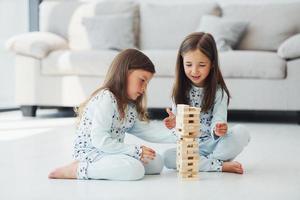 Playing tower game. Two cute little girls indoors at home together. Children having fun photo