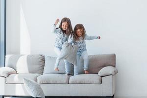 Pillow fight. Two cute little girls indoors at home together. Children having fun photo
