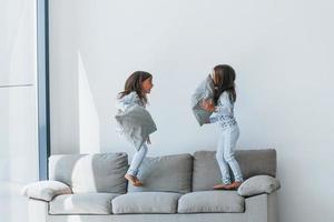 Pillow fight. Two cute little girls indoors at home together. Children having fun photo