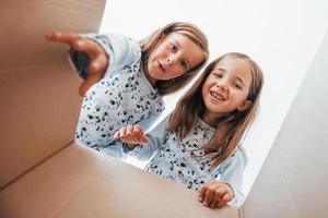 Looking inside of paper box. Two cute little girls indoors at home together. Children having fun photo