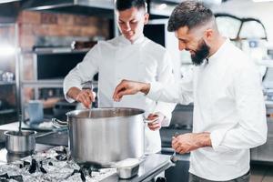 With help from other employee. Chef in white uniform cooking food at kitchen. Busy day at work photo