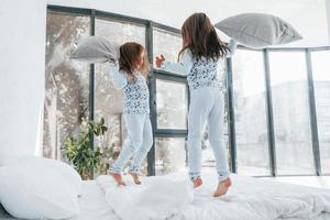 Pillow fight. Two cute little girls indoors at home together. Children having fun photo
