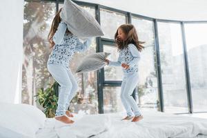 Pillow fight. Two cute little girls indoors at home together. Children having fun photo