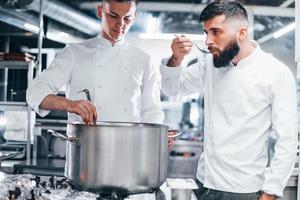 With help from other employee. Chef in white uniform cooking food at kitchen. Busy day at work photo