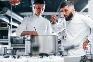 With help from other employee. Chef in white uniform cooking food at kitchen. Busy day at work photo