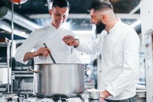 With help from other employee. Chef in white uniform cooking food at kitchen. Busy day at work photo