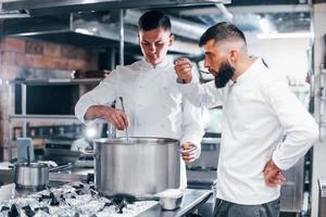 With help from other employee. Chef in white uniform cooking food at kitchen. Busy day at work photo