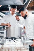 With help from other employee. Chef in white uniform cooking food at kitchen. Busy day at work photo