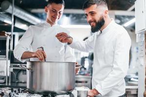 With help from other employee. Chef in white uniform cooking food at kitchen. Busy day at work photo