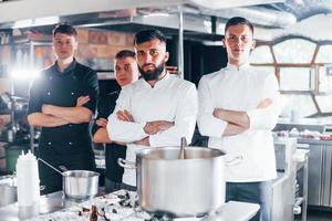 Group of people in white uniform standing together at kitchen. Cooking food photo